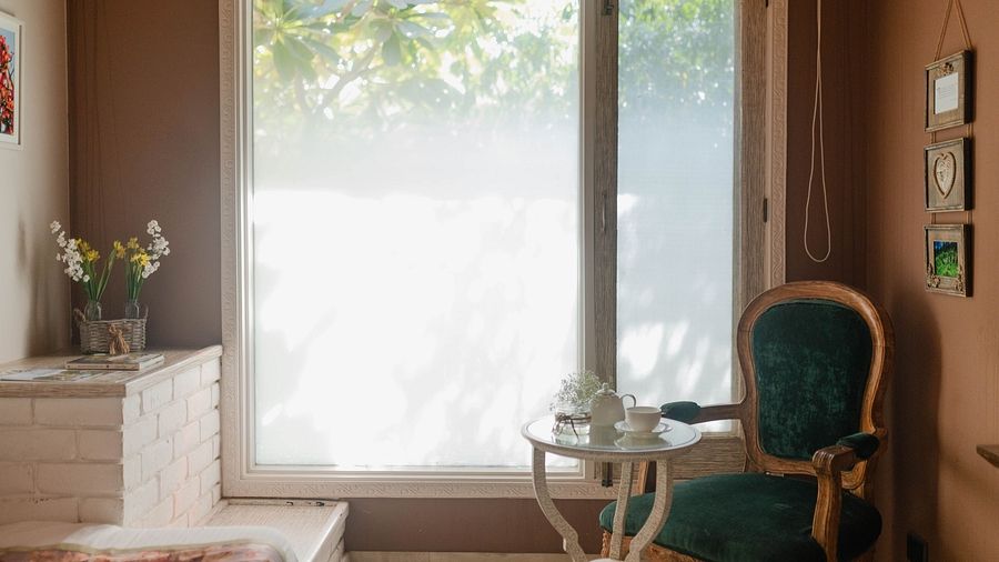 A bedroom at Karma Chalets with a window, green chair, white drawers, and a vase with flowers.