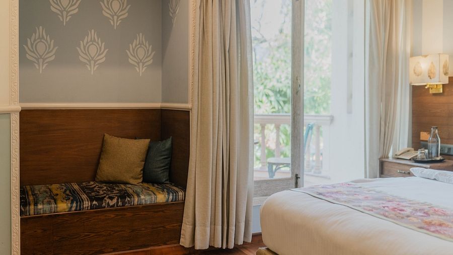 A bedroom at Karma Chalets with a bed, a sitting area with cushions and huge windows with curtains.