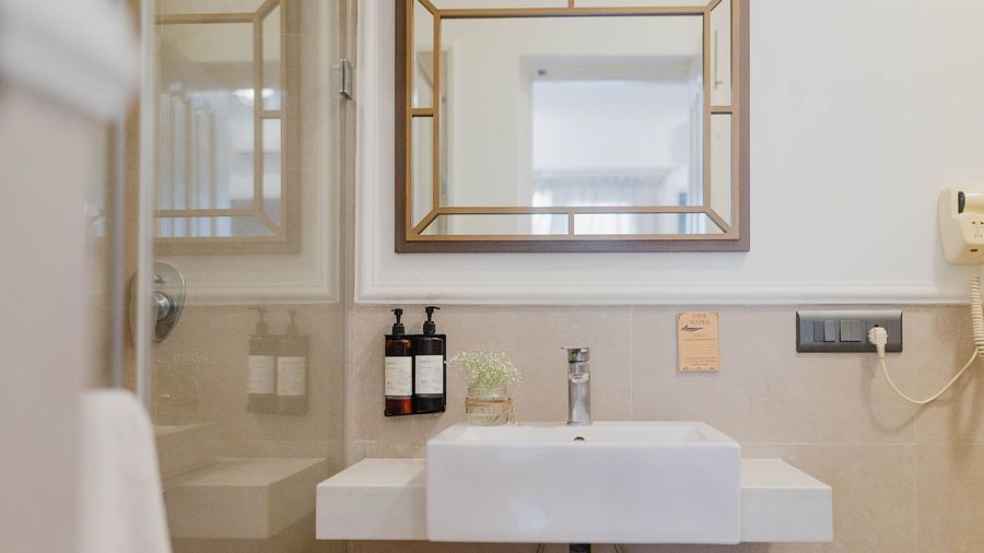 A bathroom at Karma Chalets with a white sink, mirror, soap dispensers, and grey-tiled walls.