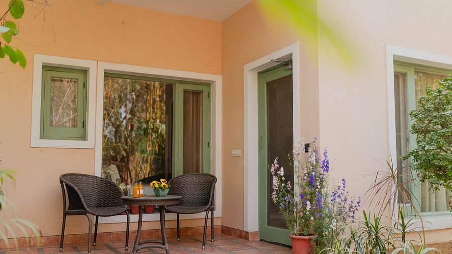 Exterior of a Karma Chalets unit with two chairs and a table on a tiled porch, surrounded by plants.