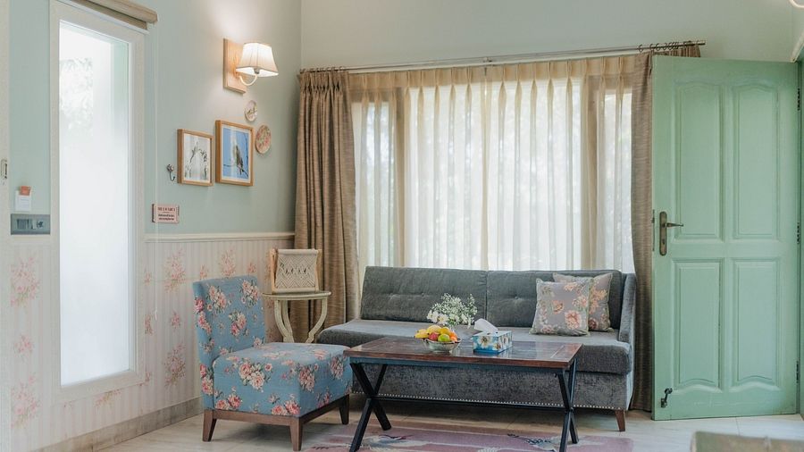 A sitting area at Karma Chalets with a grey sofa, armchair, coffee table, and large window with curtains.
