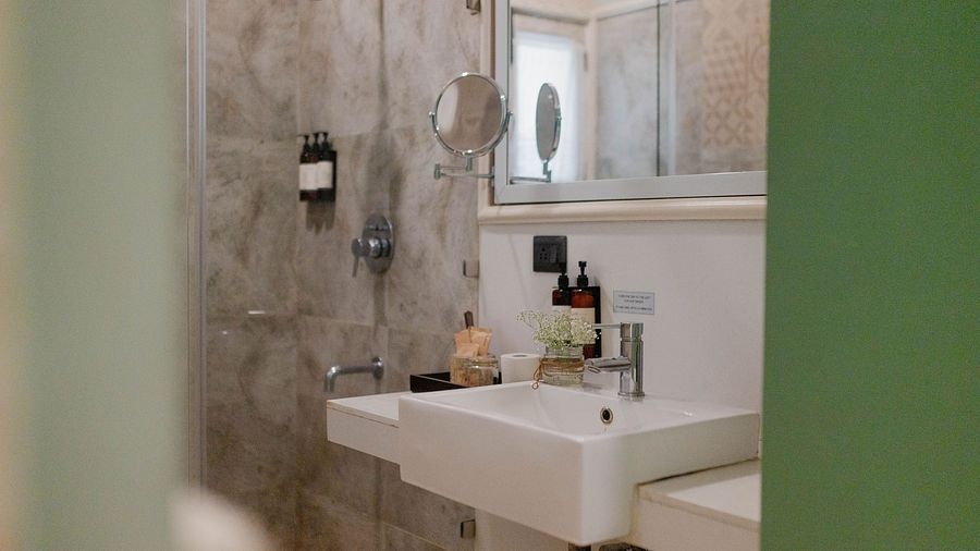 A bathroom at Karma Chalets with a white sink, mirror, soap dispensers, and grey-tiled walls.