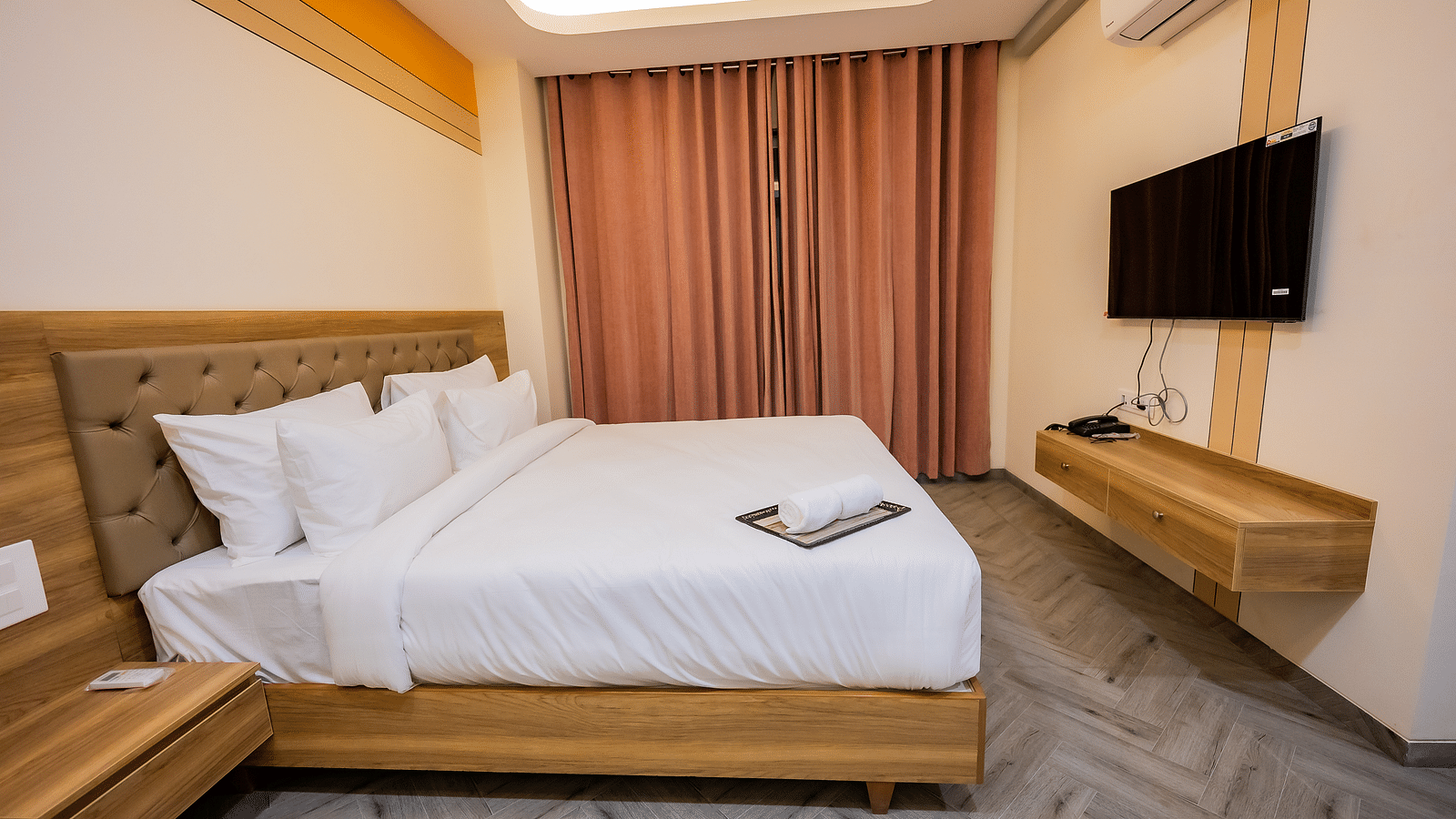 A modern hotel room at Lotus Leaf Boutique Hotel with a large bed, curtains, and a mounted TV.