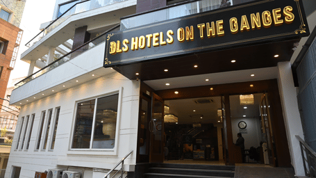 Front entrance of DLS Hotels on the Ganges, showing the wide staircase leading to the lobby, the glass doors, and the hotel signage prominently displayed above, welcoming guests to a comfortable stay