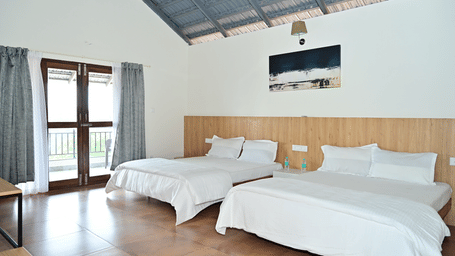 A room at Hilllock Vista Homestay by Aarika Resorts, with two beds, pillows, spreads, and a door leading to a balcony.