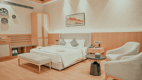 A luxurious hotel room with a large, neatly made bed, a bench at the foot of the bed, and an armchair next to a round table.