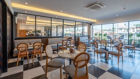 Side shot of a bar at Vishranti Hotel Dehradun with chairs, tables, a counter and checkered floors. 
