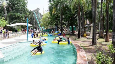 People enjoy a lazy river ride in a water park, surrounded by palm trees and greenery.
