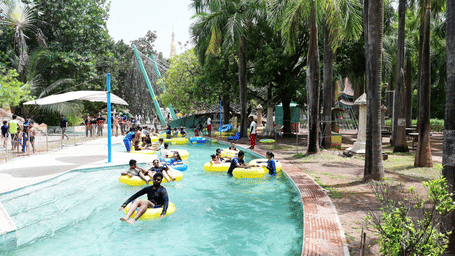 People enjoying a lazy river ride in a Water Kingdom, surrounded by palm trees and greenery. Water Kingdom is one of the fun places in Mumbai, instead of Goa to visit, with it's rides and chilled atmosphere.