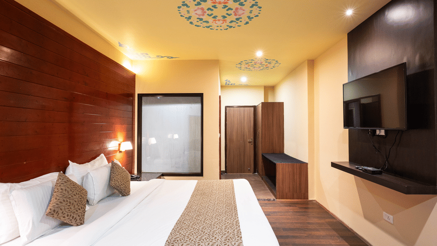 A bedroom featuring a patterned ceiling art and a wall-mounted television at Avianna Hungry Jack, Gangtok.