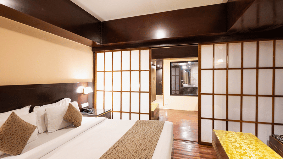 A bedroom with a comfortable bed, sliding doors, and warm lighting leading to another room at Avianna Hungry Jack, Gangtok.
