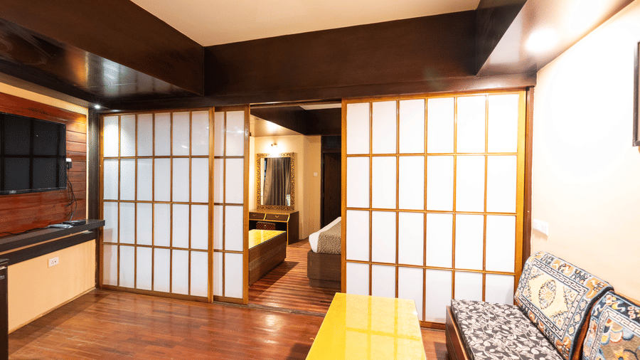 A room with wooden flooring, a cozy seating area, and sliding doors leading to a bedroom at Avianna Hungry Jack, Gangtok.