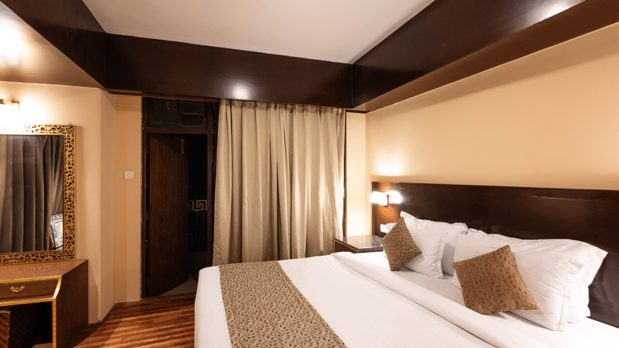A bedroom with a large bed, bedside lamps, and a mirror near a closed curtain window at Avianna Hungry Jack, Gangtok.