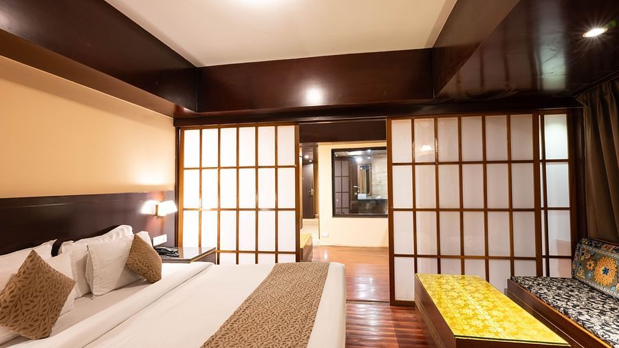 A bedroom with a large bed, sliding doors, and a cushioned seating area near a table at Avianna Hungry Jack, Gangtok.
