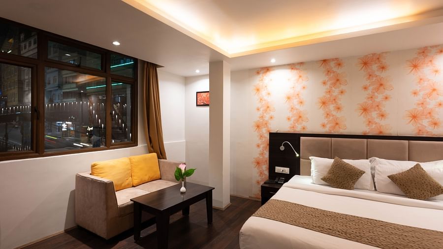 A bedroom with a small table holding a flower vase and an open curtain window at Avianna Hungry Jack, Gangtok.