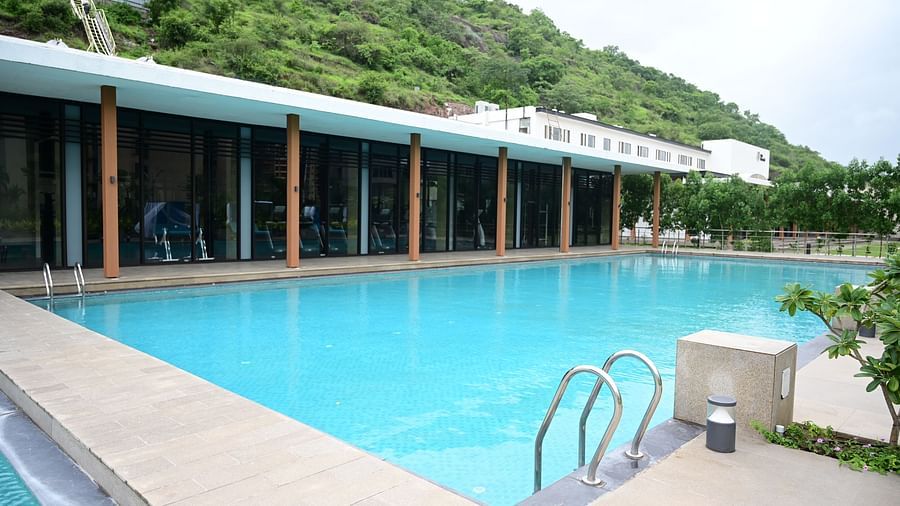close up image of the swimming pool with the restaurant on the poolside at club charholi, pune