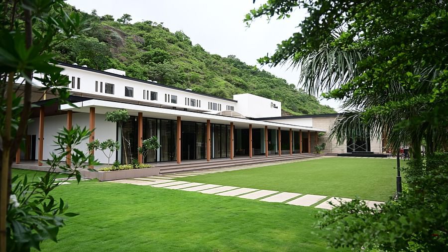 A modern building with a long, covered porch , backed by a wooded hillside.