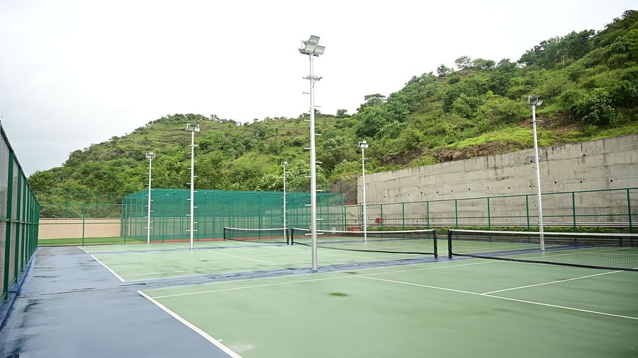 image featuring a tennis court at club charholi, pune with a lush green hill in the background