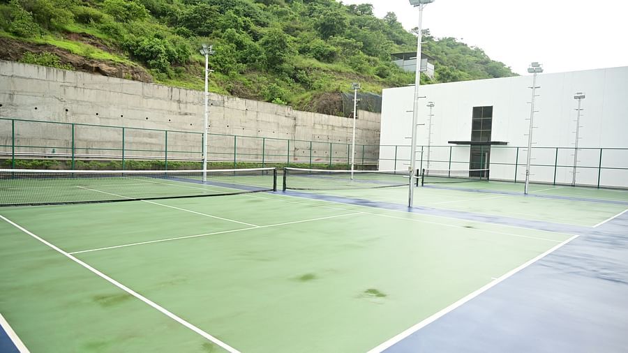 image of the the expansive tennis court with a lush green hilltop in the background of club charholi, pune