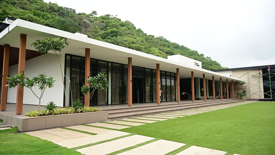 Building with a long, covered walkway, glass doors, and a pathway leading to a lawn and hillside.