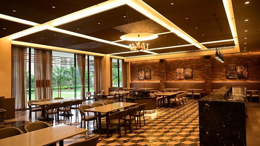 Dining area with tables, chairs, patterned floor, and textured walls, lit by ceiling lights and a chandelier, with a view to outside.