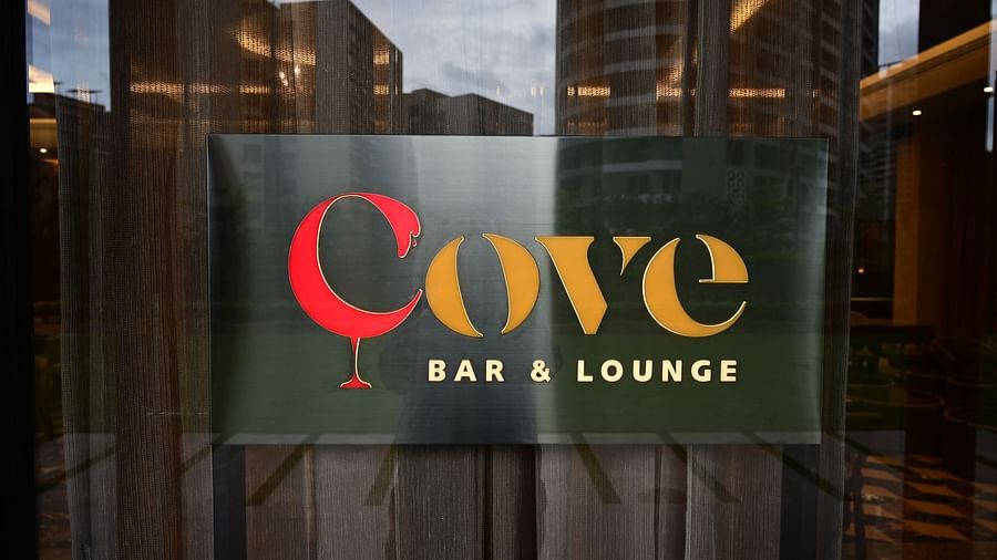 Sign for Cove BAR & LOUNGE with a stylized glass image, seen through a glass door with a city view reflected.