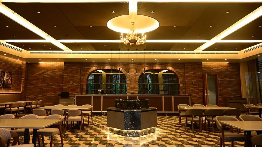 Dining room with tables, chairs, patterned floor, and textured walls, lit by ceiling lights and a chandelier.