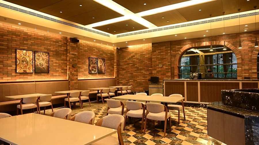 Dining area with tables, chairs, patterned floor, and textured walls, lit by ceiling lights.