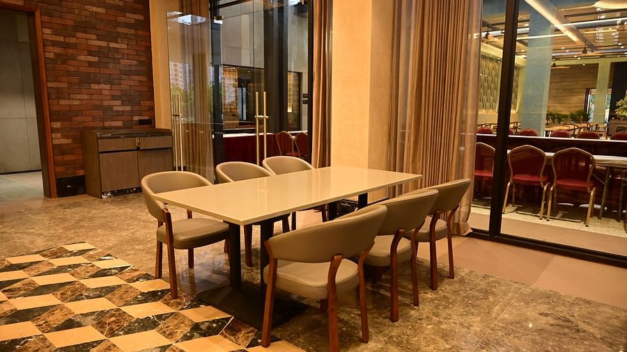Dining table with chairs in a room with patterned floor and textured walls, view through window.