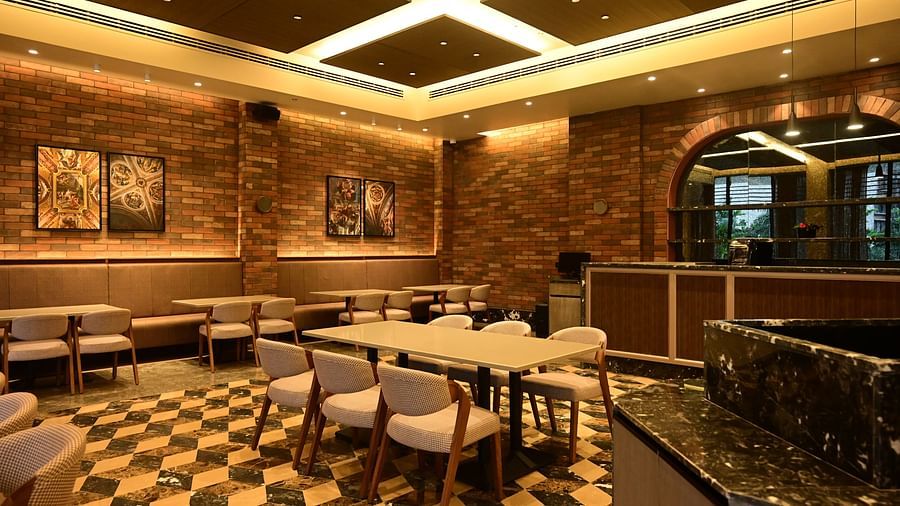 Dining area with tables, chairs, patterned floor, and textured walls, lit by ceiling lights.