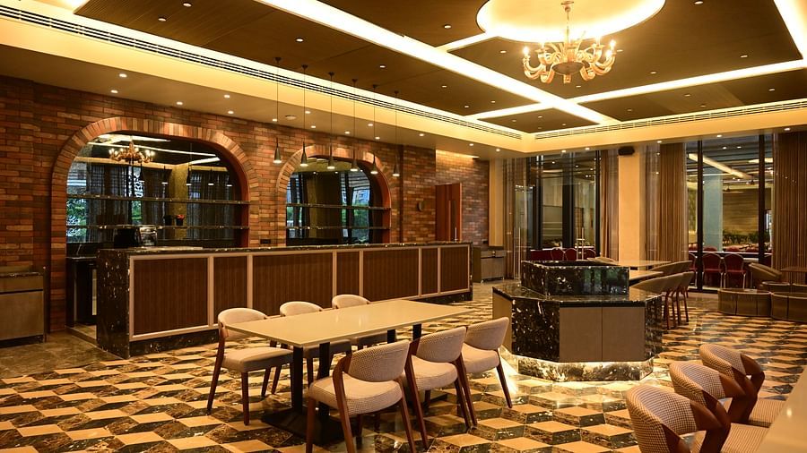 Dining area with tables, chairs, patterned floor, and textured walls, lit by ceiling lights and a chandelier.