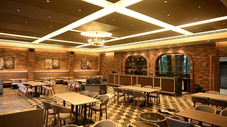Dining area with multiple tables and chairs, patterned floor, and textured walls, lit by ceiling lights and a chandelier.