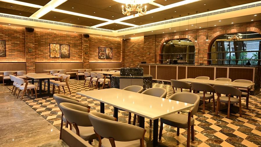 Dining area with tables, chairs, patterned floor, and textured walls, lit by ceiling lights and a chandelier.