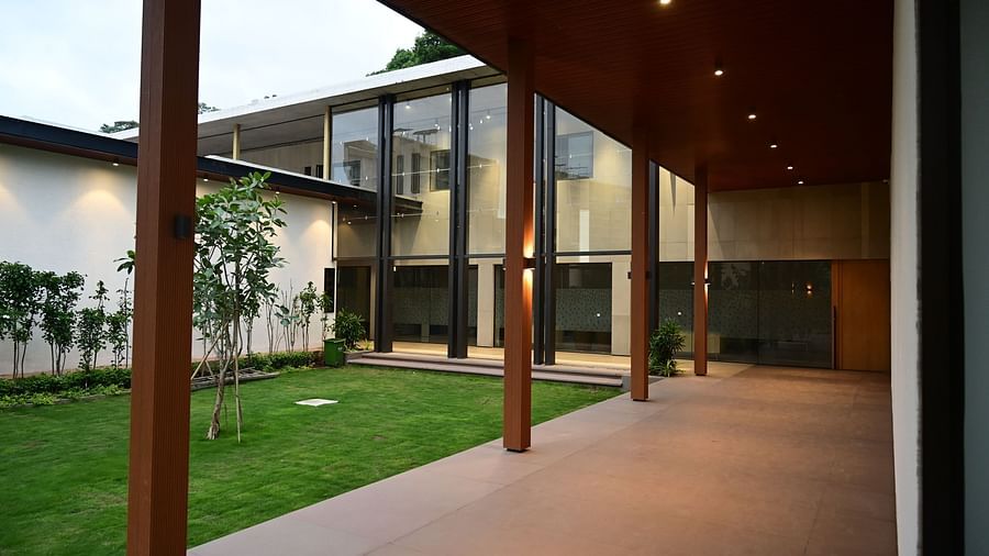 Building with a long porch, glass walls, and a green lawn, viewed from a covered walkway.