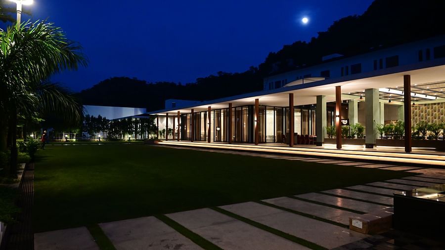Building with long porch, lit pathway, and lawn at night under a dark sky with a moon.