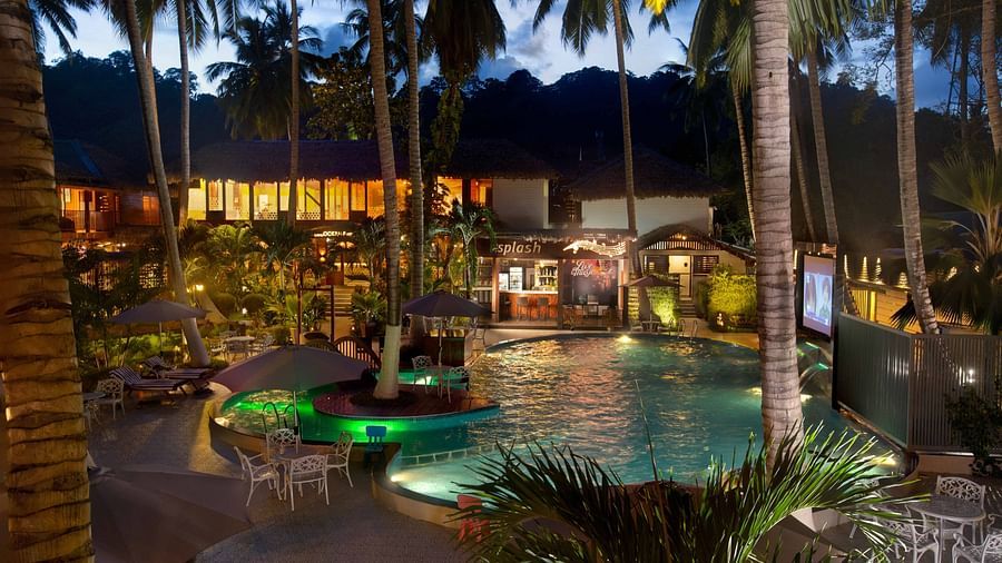  A night-time view of a resort pool area, illuminated by soft lighting. Palm trees surround the pool, creating a tropical and inviting atmosphere - Coral Reef Resort & Spa, Havelock