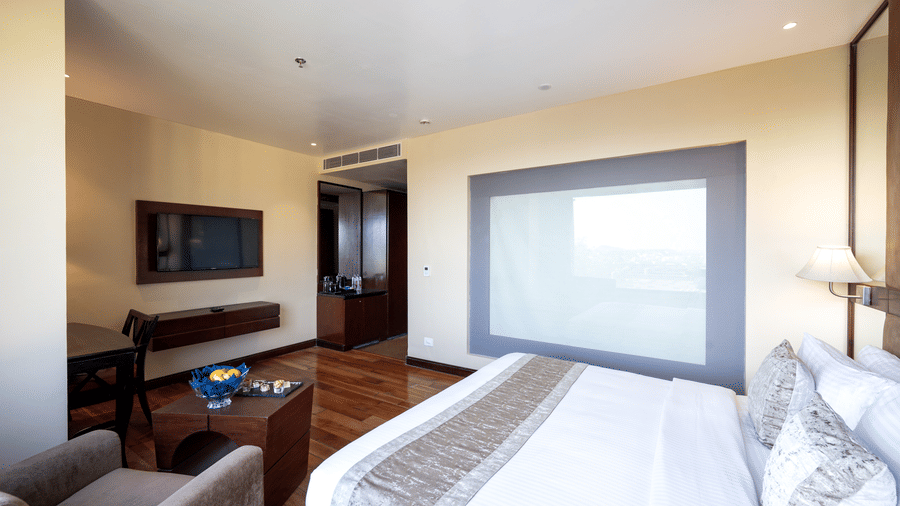 Premium Room featuring a plush bed facing the TV on the wall and a seating space at its foot at Essentia Luxury Resort & Spa, Udaipur