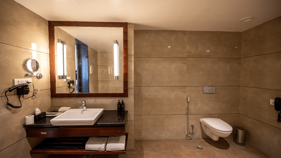 Bathroom of Premium Room at Essentia Luxury Resort & Spa, Udaipur featuring a large mirror on the wall over a sink and towels folded under it on the shelf and toilet near it