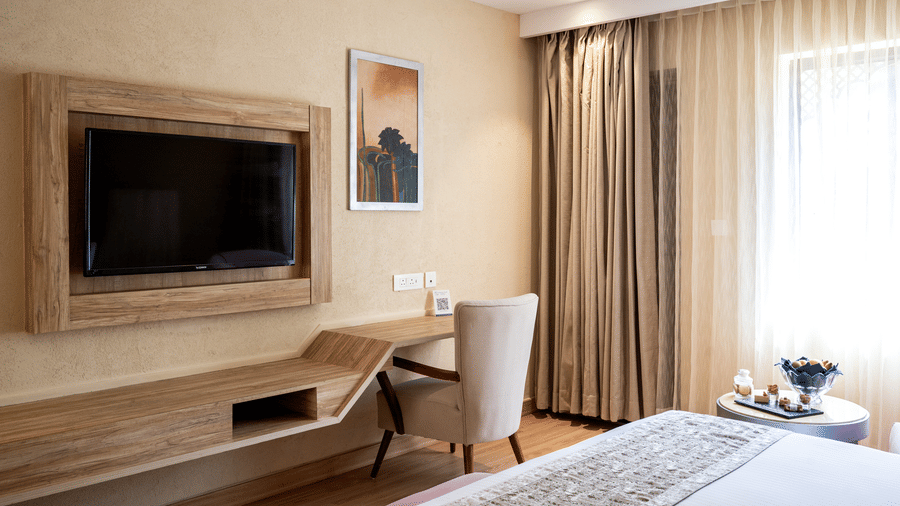 Standard Room at Essentia Luxury Resort & Spa, Udaipur featuring a bed facing the TV on the wall over a running work desk with a chair facing the wall near the window