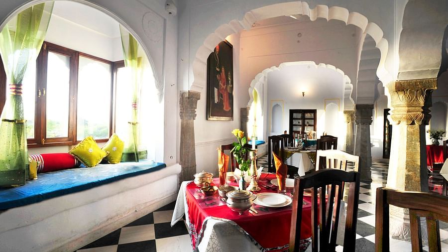 A bright dining area at Fort Barli, featuring arched doorways, checkered floors, and a window seat, blends architectural charm with a cosy meal setting.