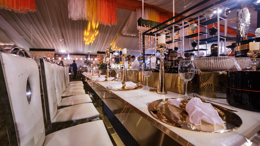 A long, formal buffet setup with catering dishes and serving equipment under event lighting in a temporary tent at Hotel Hukam's Lalit Mahal.