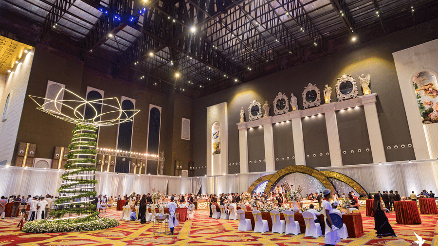 Vast, high-ceilinged convention or banquet hall decorated for an event with a large hanging ornament and a crowd of people at Hotel Hukam's Lalit Mahal.