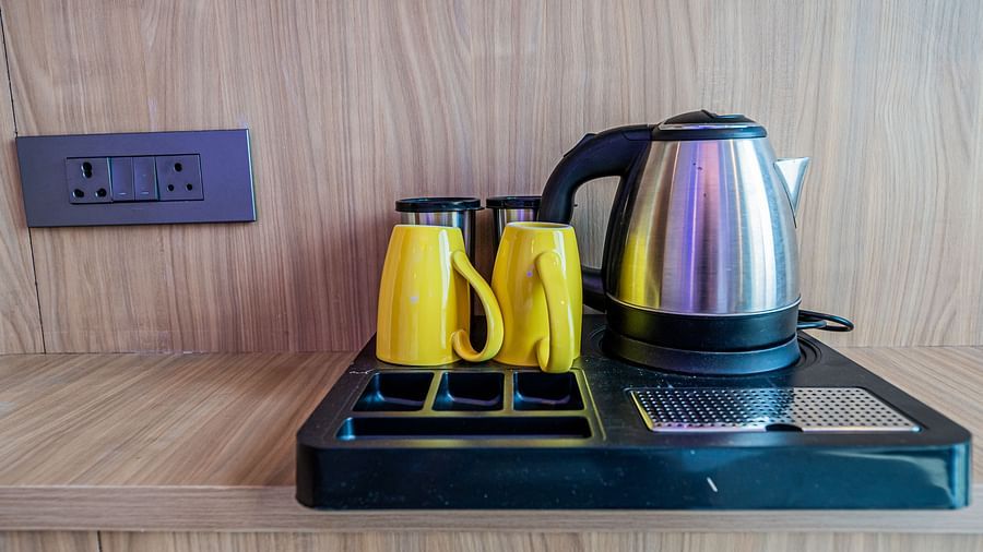 A tray placed on a wooden surface at Indie Stays Mumbai International Airport holds a kettle and cups, with a switchboard nearby.