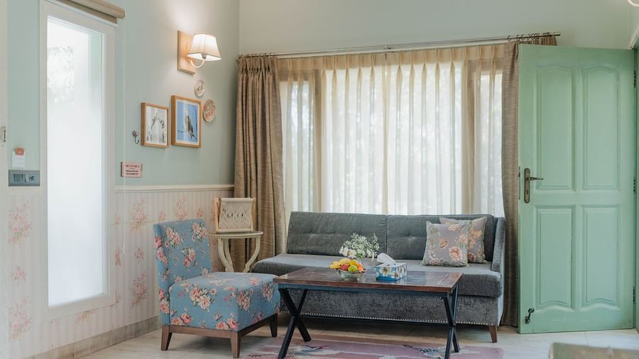 A sitting area at Karma Chalets with a grey sofa, armchair, coffee table, and large window with curtains.