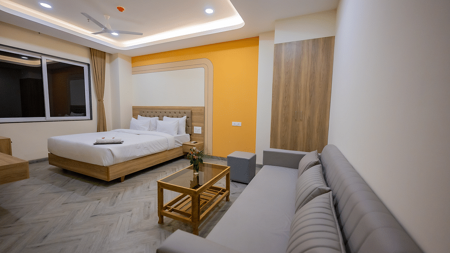 A view of a hotel room with a clean, white bed, a wooden nightstand, and large windows with natural light