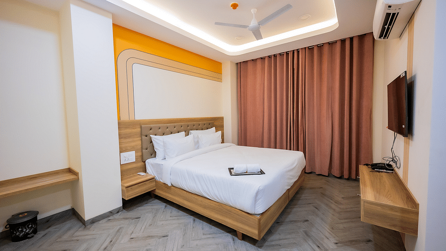 A cosy hotel room with soft lighting, a bed, curtains, and a TV mounted on the wall.