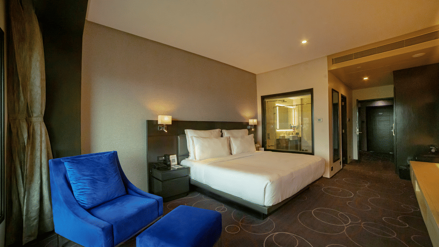 Hotel room featuring a double bed and a blue lounge chair with a leg rest – Narayani Heights Hotel & Resorts