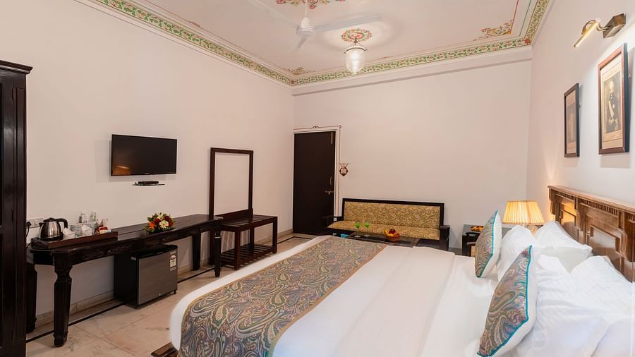 A spacious bedroom view from the headboard at Panna Vilas Palace, showcasing a wall-mounted television with a wooden table positioned below it | Panna Vilas Udaipur
