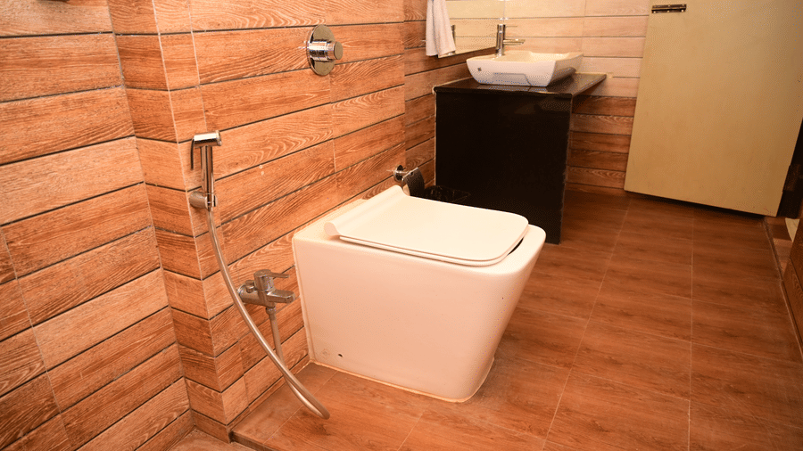 The modern bathroom featuring a white square toilet, a dark vanity, and walls with wooden panelling or tiling in a reddish-brown tone at Pipul Odi Art Museum Resort.