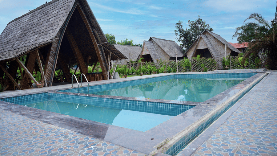 Resort's outdoor area, showing the swimming pool with its surrounding deck and several A-frame cottages under a blue sky at Pipul Odi Art Museum Resort.